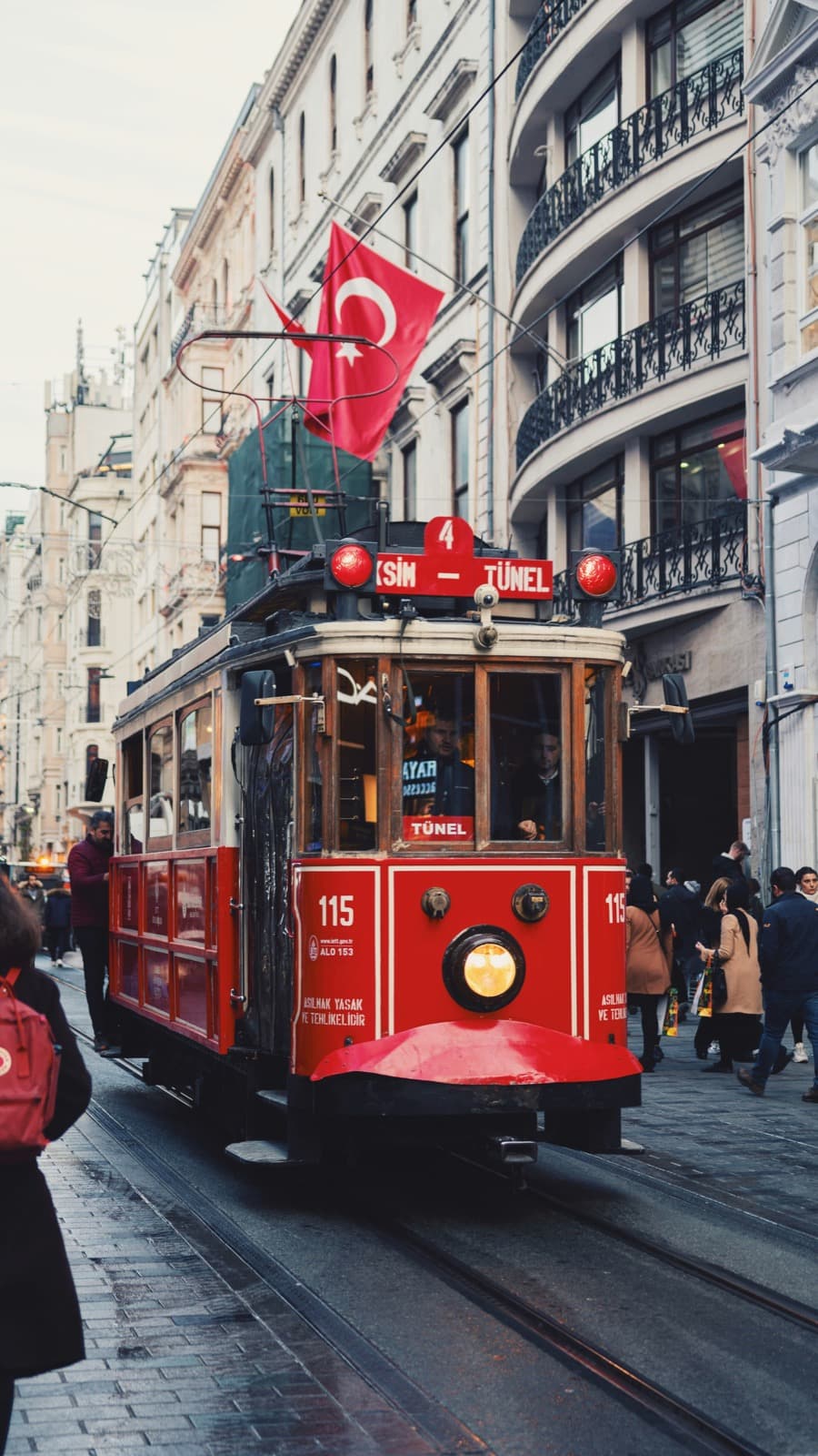 The red Taksim–Tünel heritage tram on İstiklal Street, Istanbul, under a Turkish flag
