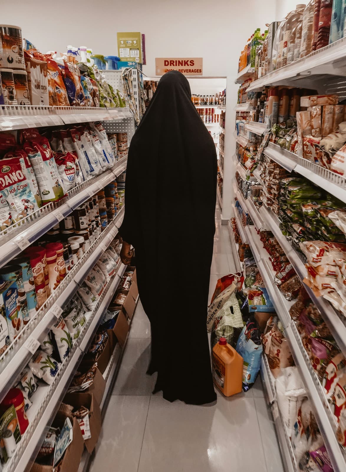 A shopper in a black abaya choosing goods along a supermarket aisle